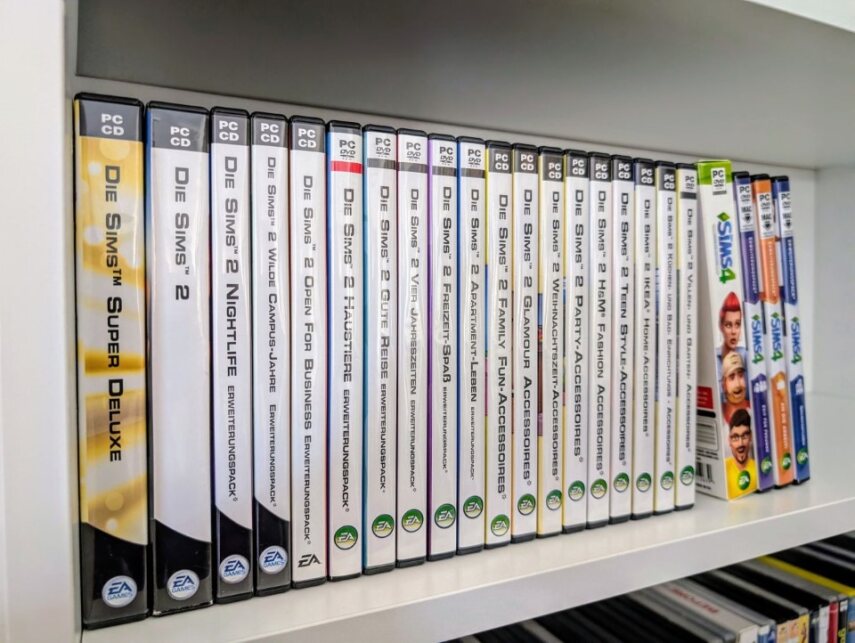 Das Foto zeigt ein Regal, in dem eine ganze Reihe von Computerspielen steht. Alle Verpackungen sind verschiedene Teile der Reihe Sims, Sims 2 oder Sims 4.